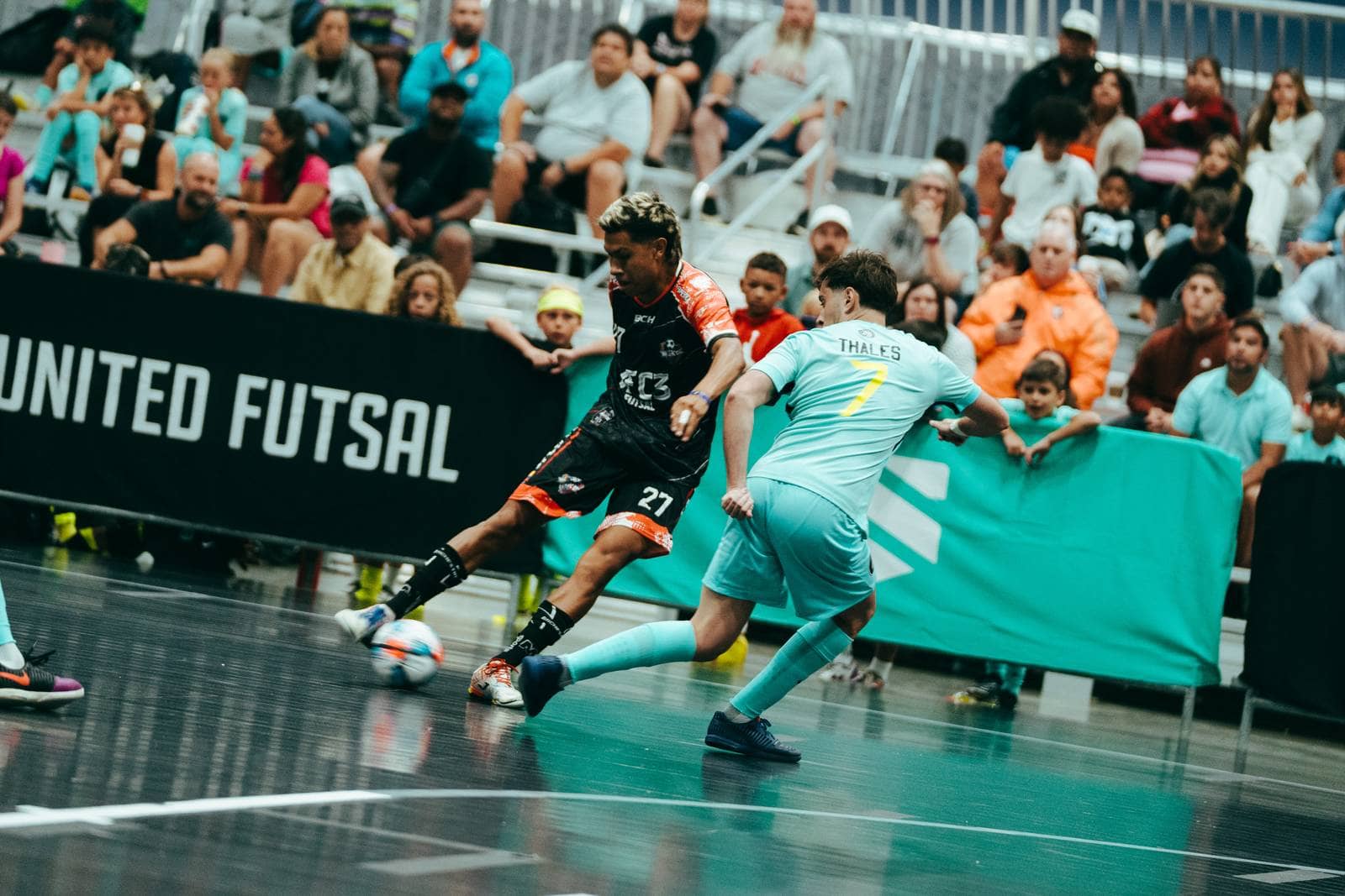 A player strikes the ball past a defender in front of a full stand